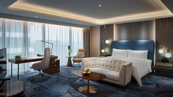 Habitación de hotel moderna con una cama grande, un escritorio, una silla y una mesita con fruta.