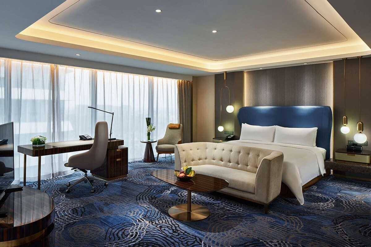A modern hotel room with a large bed, a desk, and a chair.