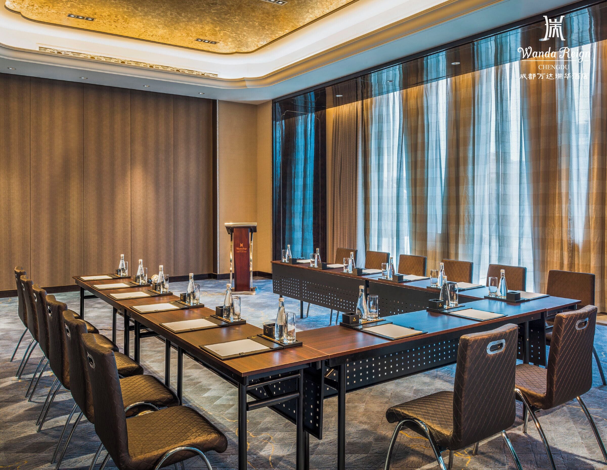 A conference room with a long table, chairs, a podium, and large windows with curtains.