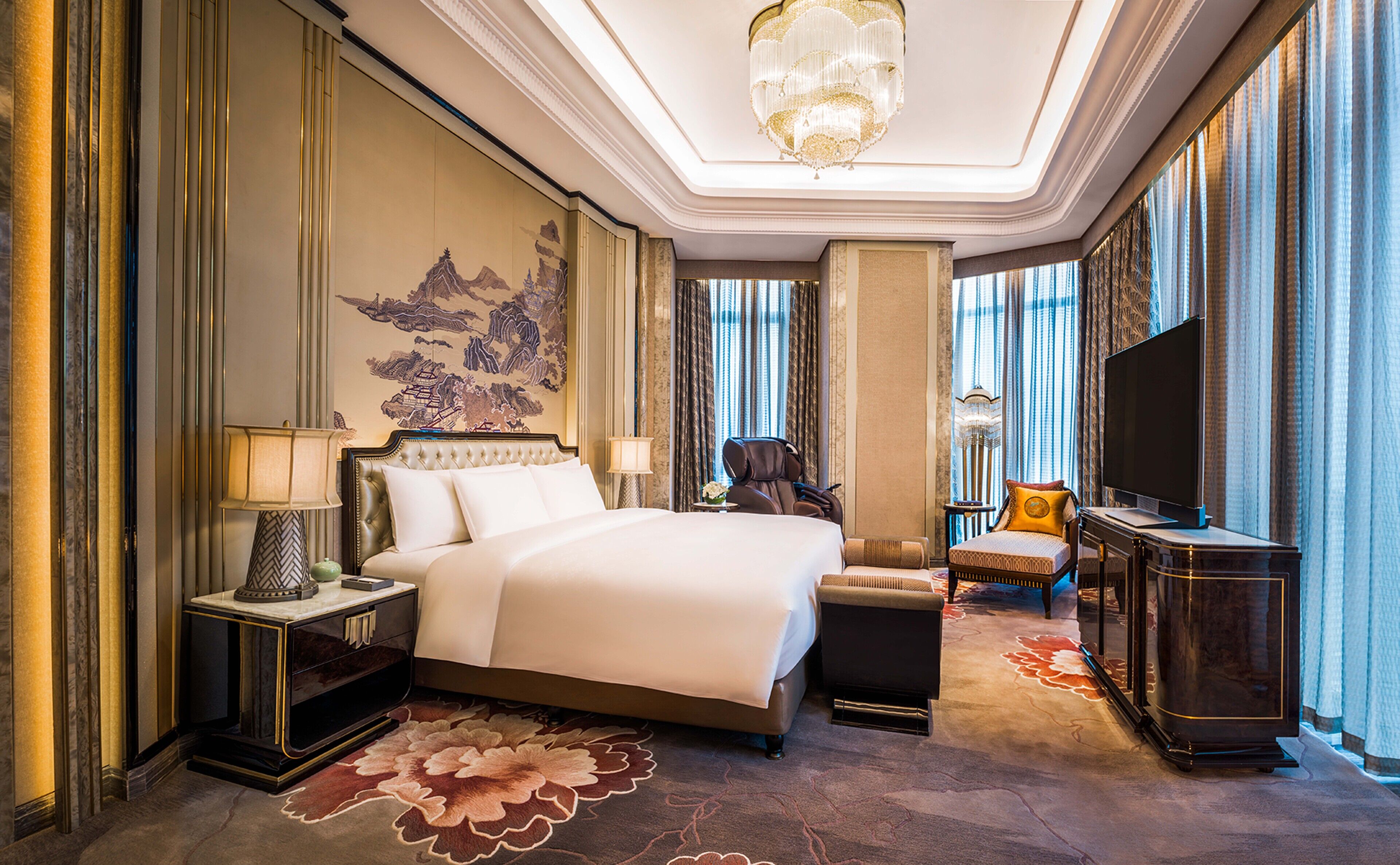 Een luxe hotelkamer met een groot bed, een massagestoel, een televisie en een decoratief wandobject.