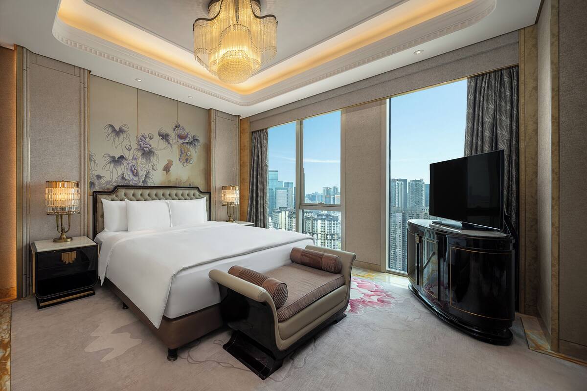 Habitación de hotel con una cama grande, un sofá, un televisor y vistas de la ciudad.