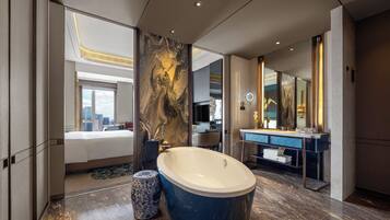 Un baño moderno con una bañera grande, un tocador con espejo y vistas a la ciudad desde el dormitorio contiguo.
