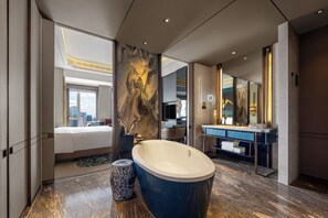 A modern bathroom with a large bathtub, a vanity with a mirror, and a city view from the adjacent bedroom.