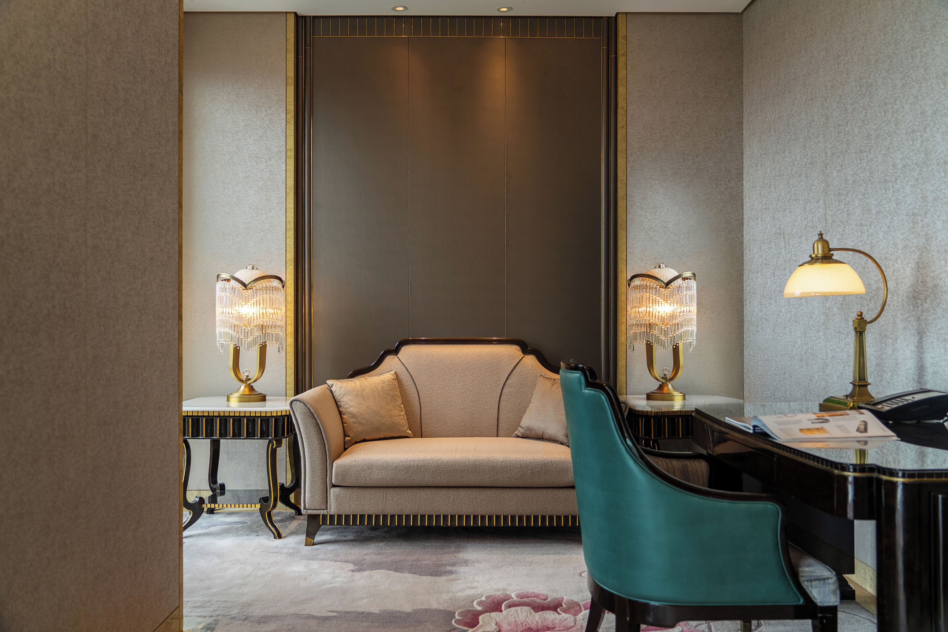 A room with a sofa, two lamps, a desk, and a chair.