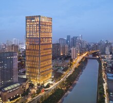 Un edificio alto de diseño moderno, rodeado por un río y otras construcciones urbanas.