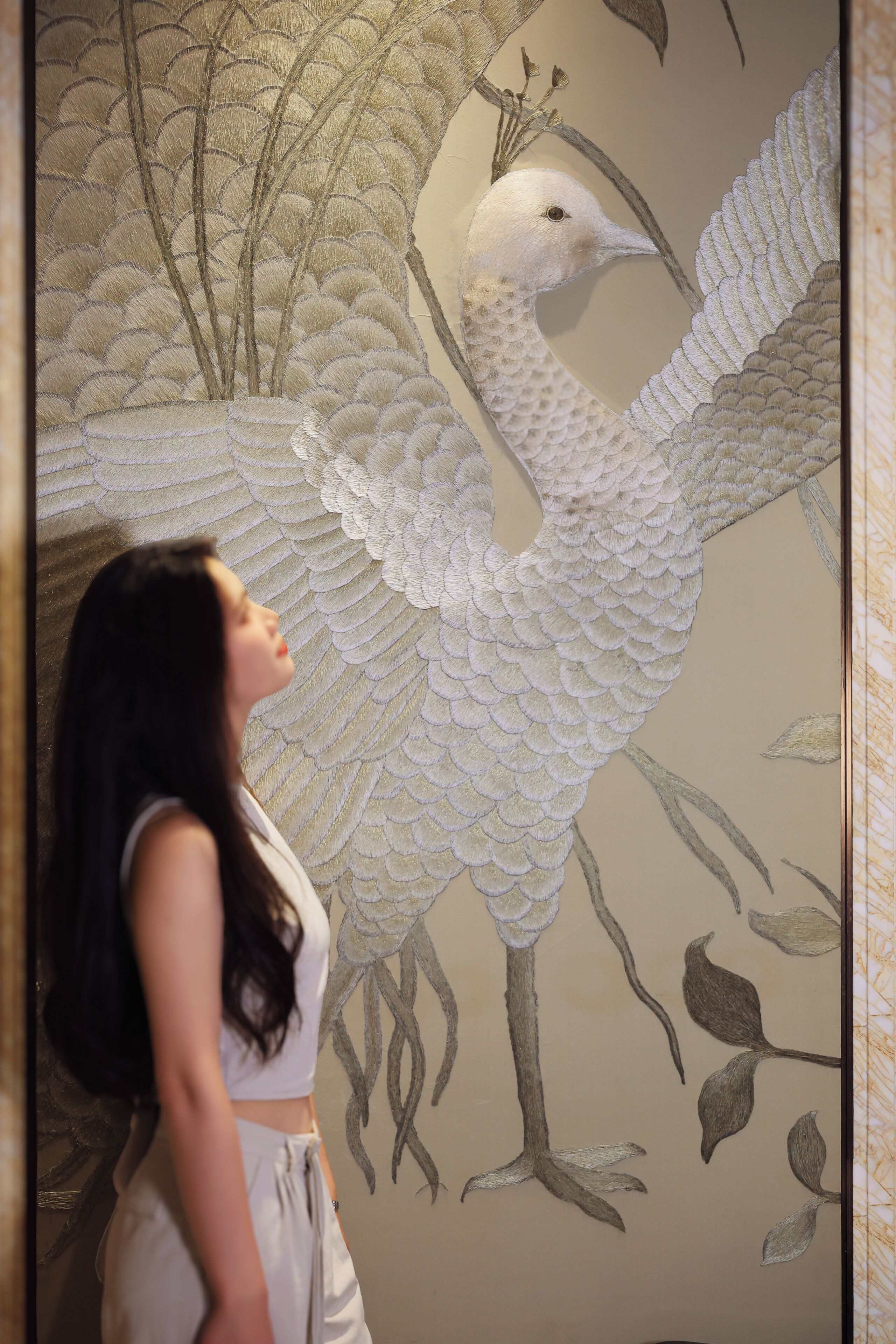 Una persona de pie frente a un muro con un mural grande y detallado de un pájaro.
