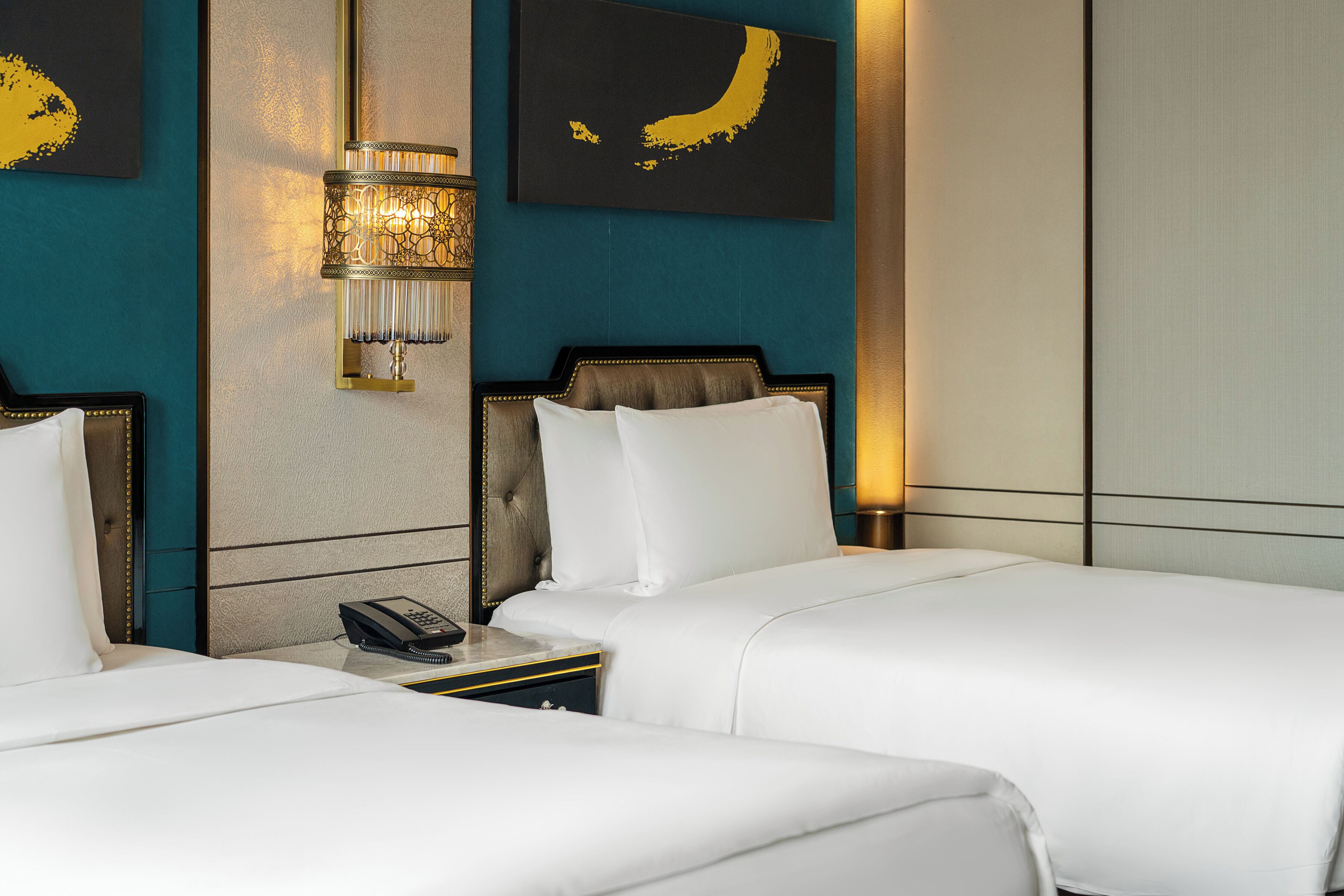 A hotel room with two beds, a nightstand with a telephone, and wall-mounted artwork.