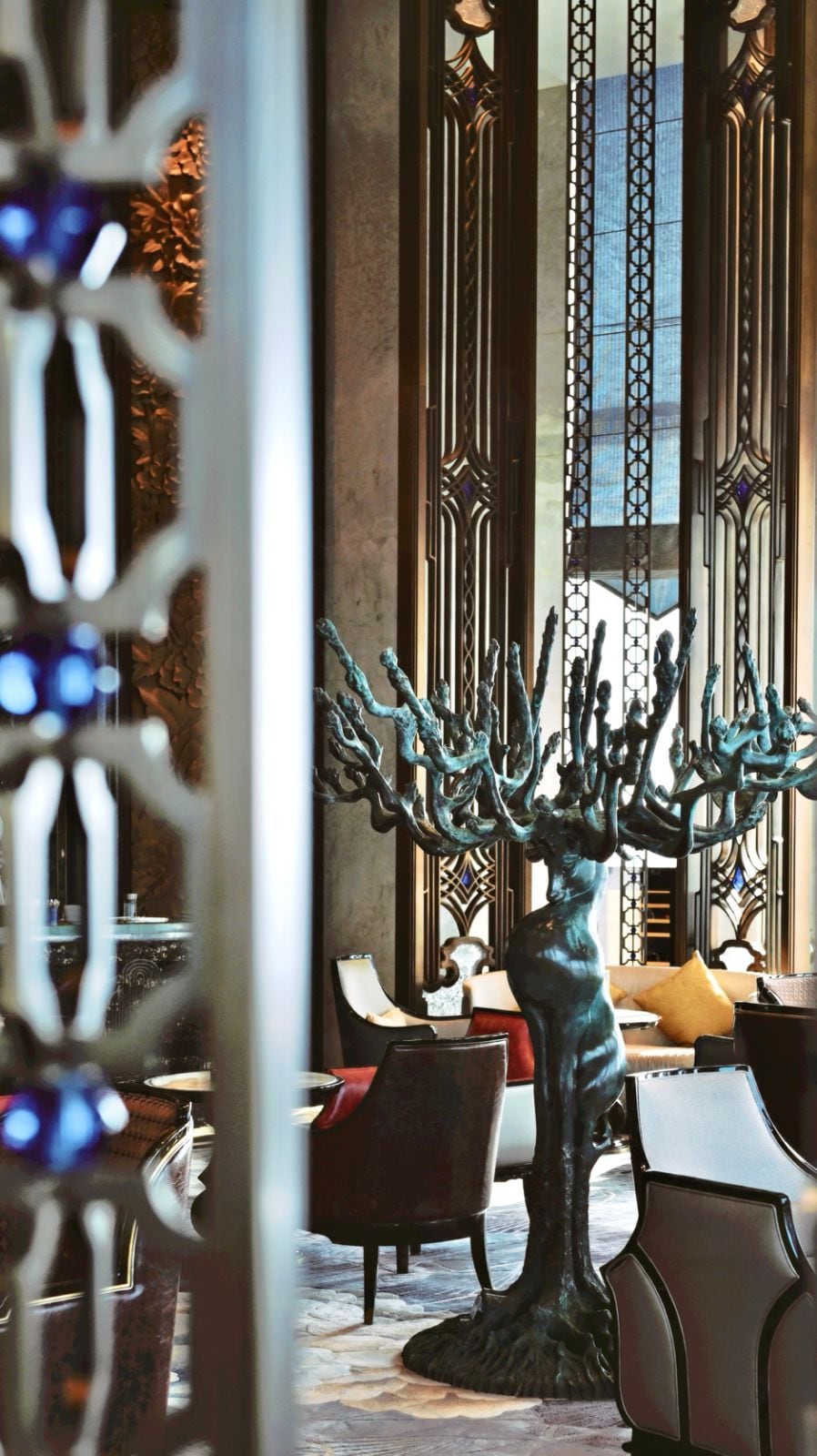 A dining area with a central sculpture, tables, chairs, and a decorative window with intricate patterns.