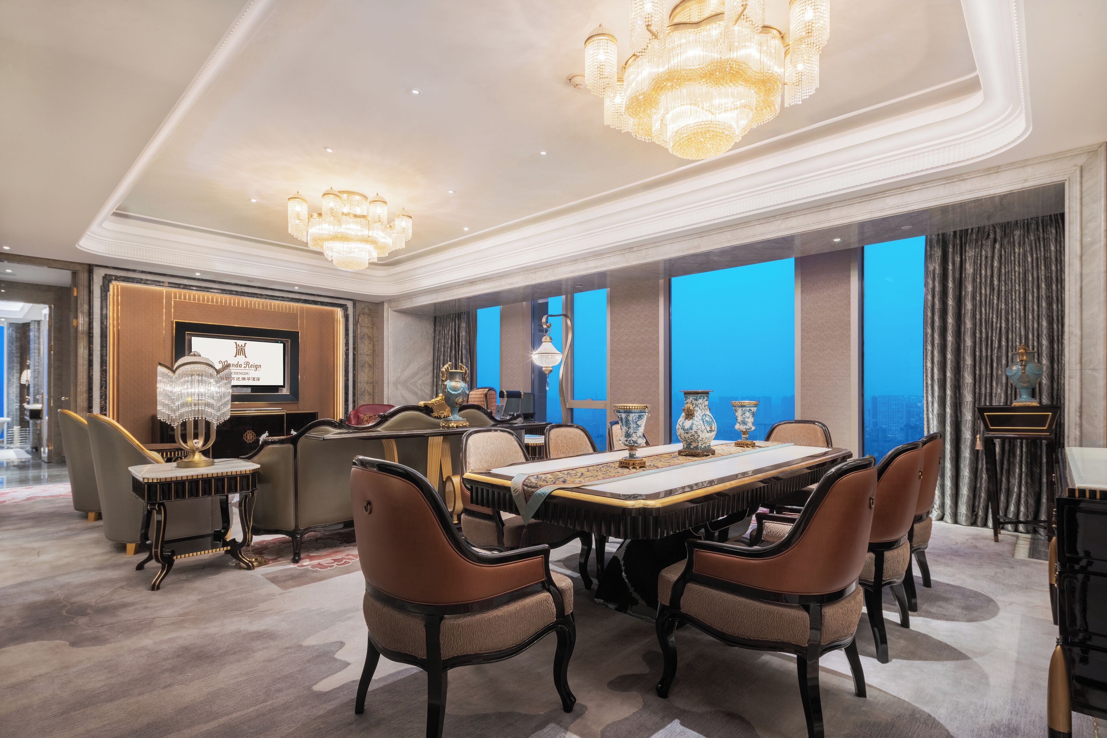 A spacious dining area with a long table, elegant chairs, and chandeliers.