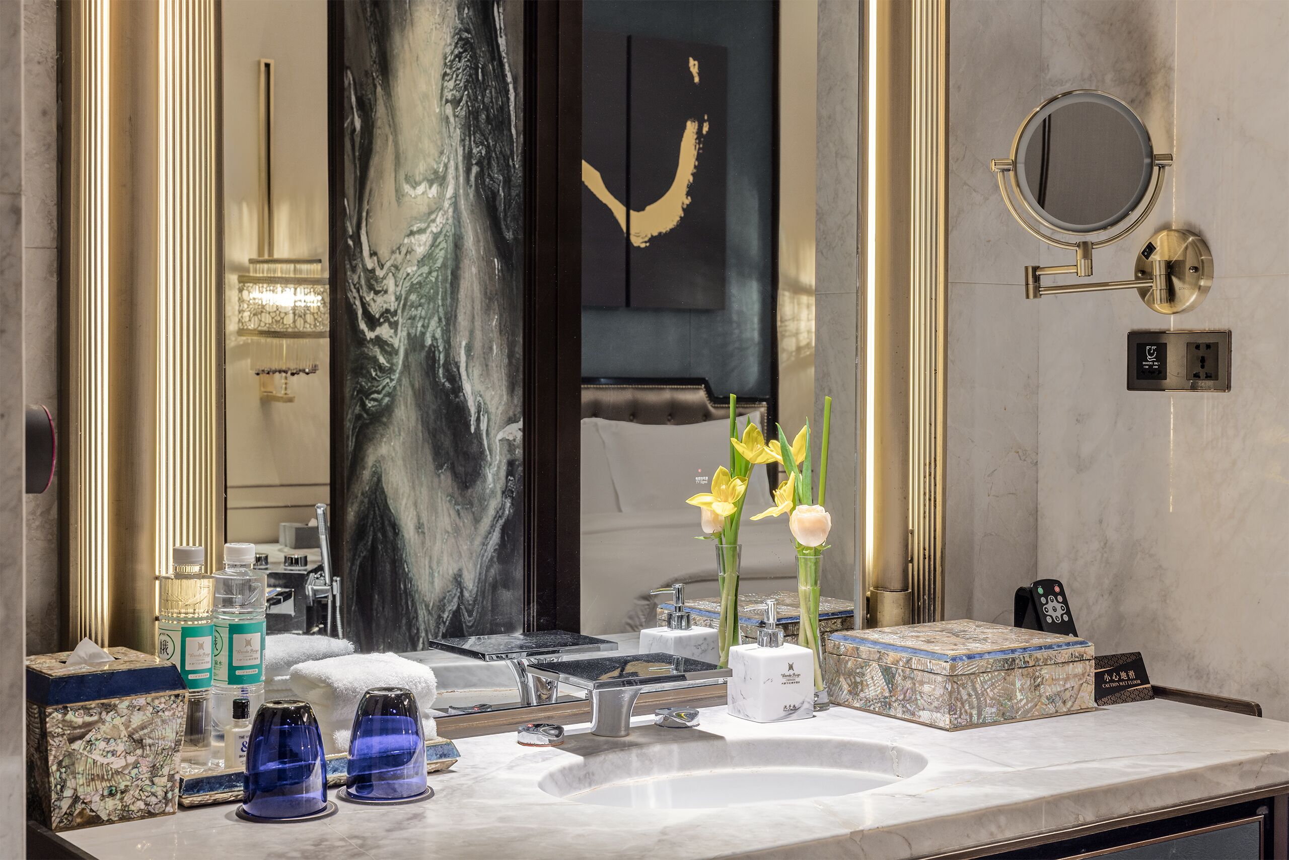 A luxurious bathroom with a marble sink, a large mirror, and a decorative vase with flowers.