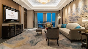 A luxurious hotel lobby with a large screen displaying the hotel name, a chandelier, a sofa, a patterned armchair, and a traditional mural. - Wanda Reign Chengdu (Chengdu)