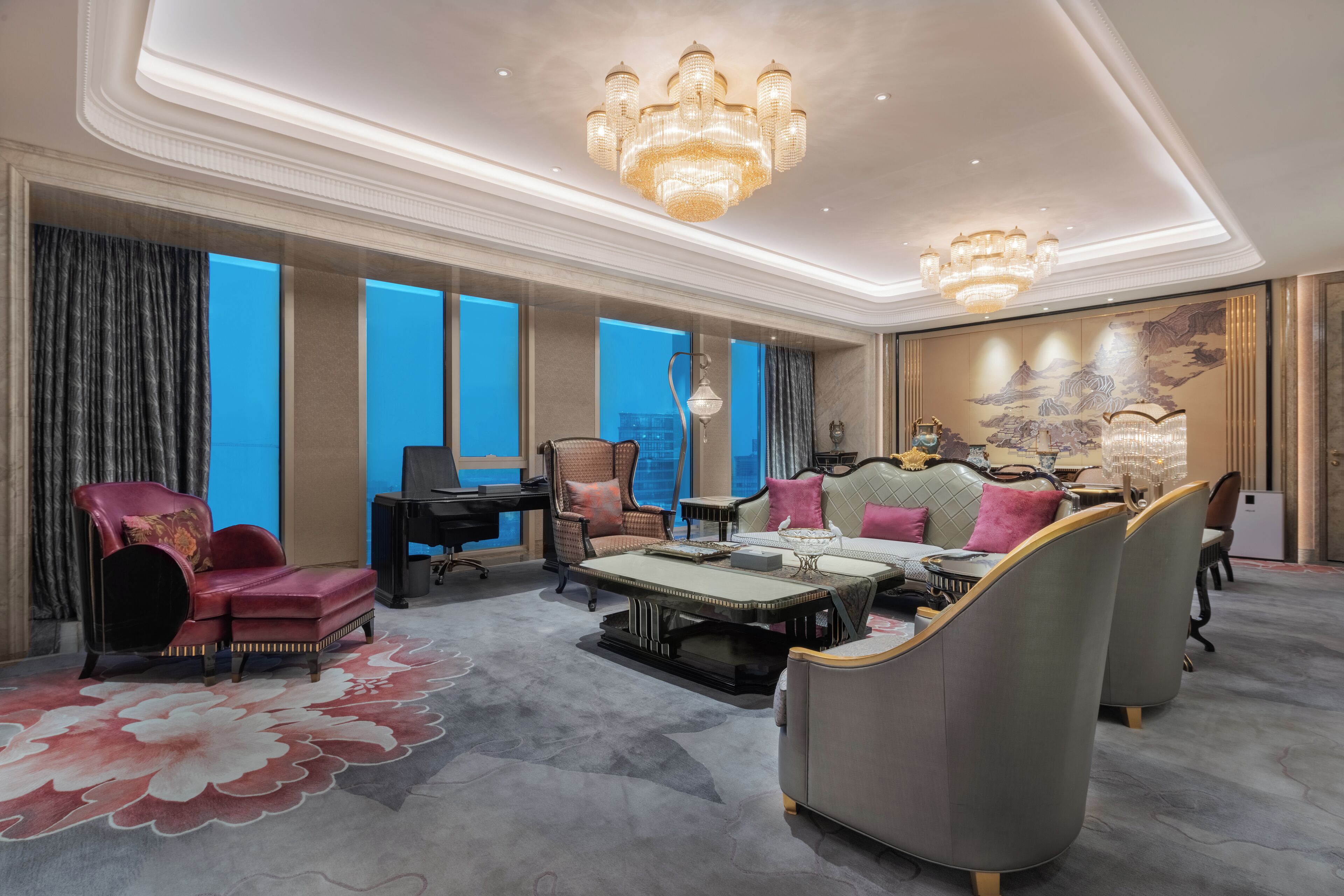 A spacious living room with a large window, a chandelier, and a traditional Chinese mural.