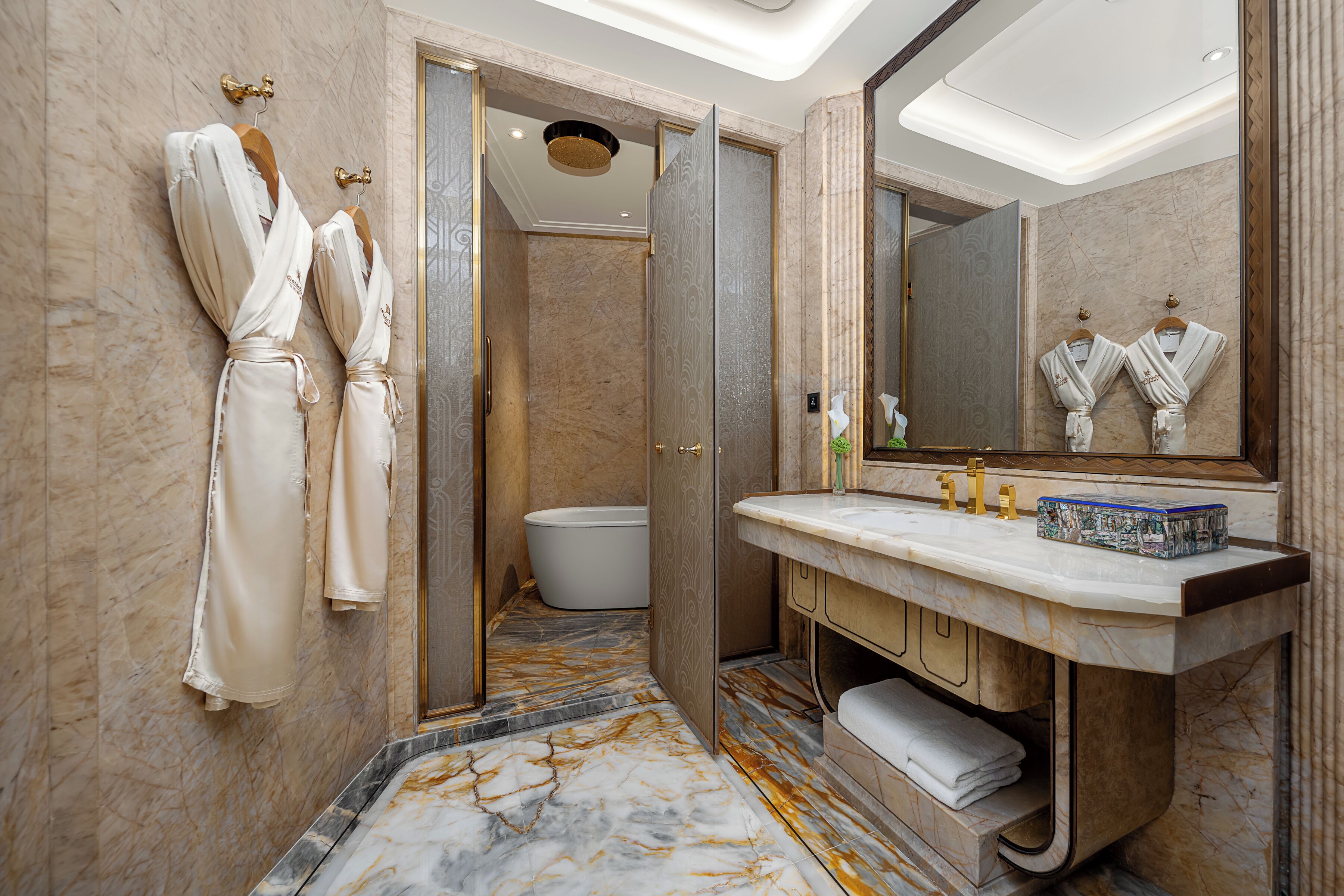 A bathroom with marble flooring, a bathtub, a vanity with a mirror, and two robes hanging on the wall.