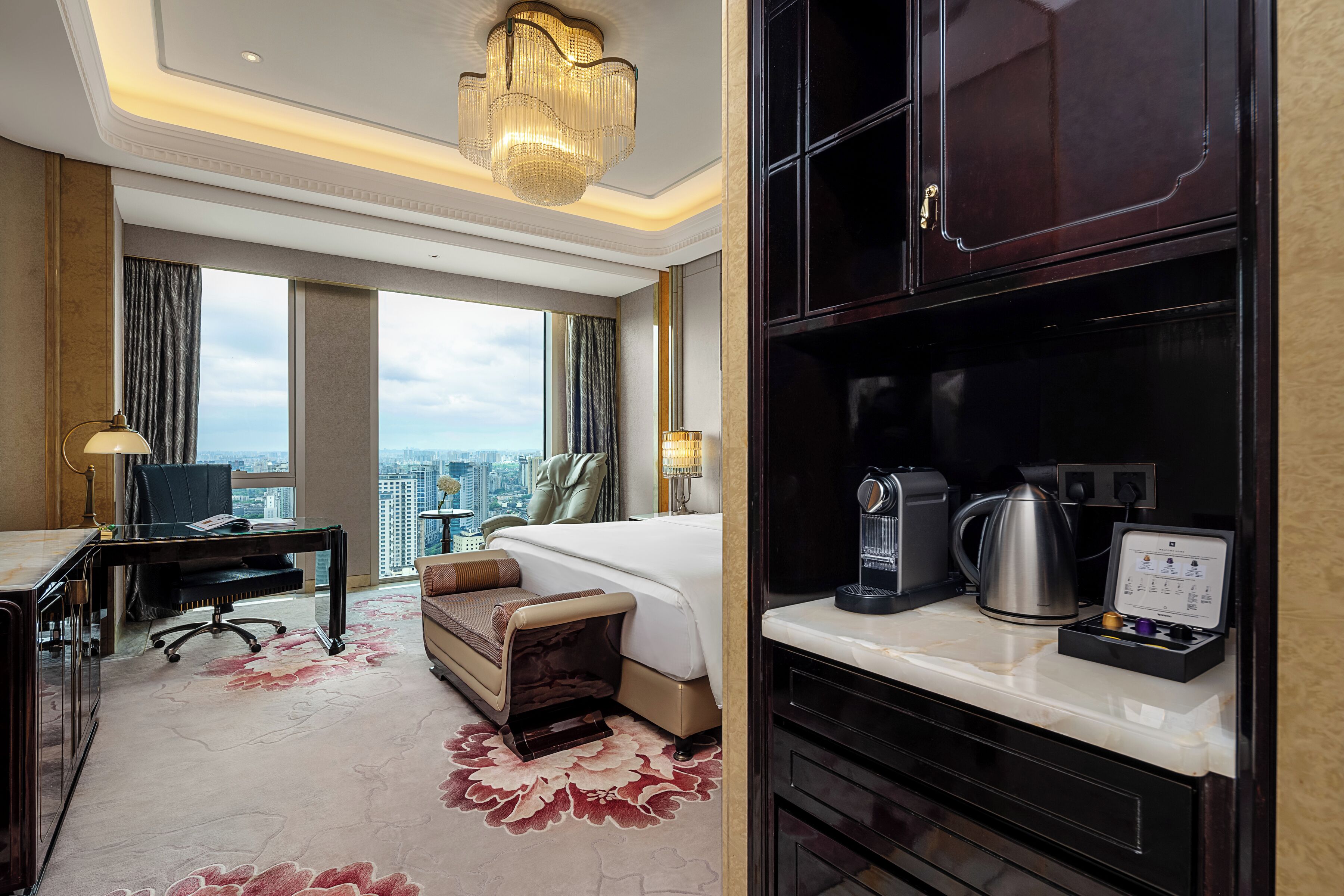 A hotel room with a large bed, a desk with a computer, a coffee maker, and a view of the city.