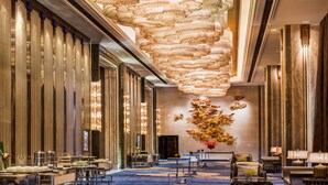 Un hall d’hôtel spacieux, doté d’un plafond haut, d’un éclairage décoratif et d’une composition florale centrale.