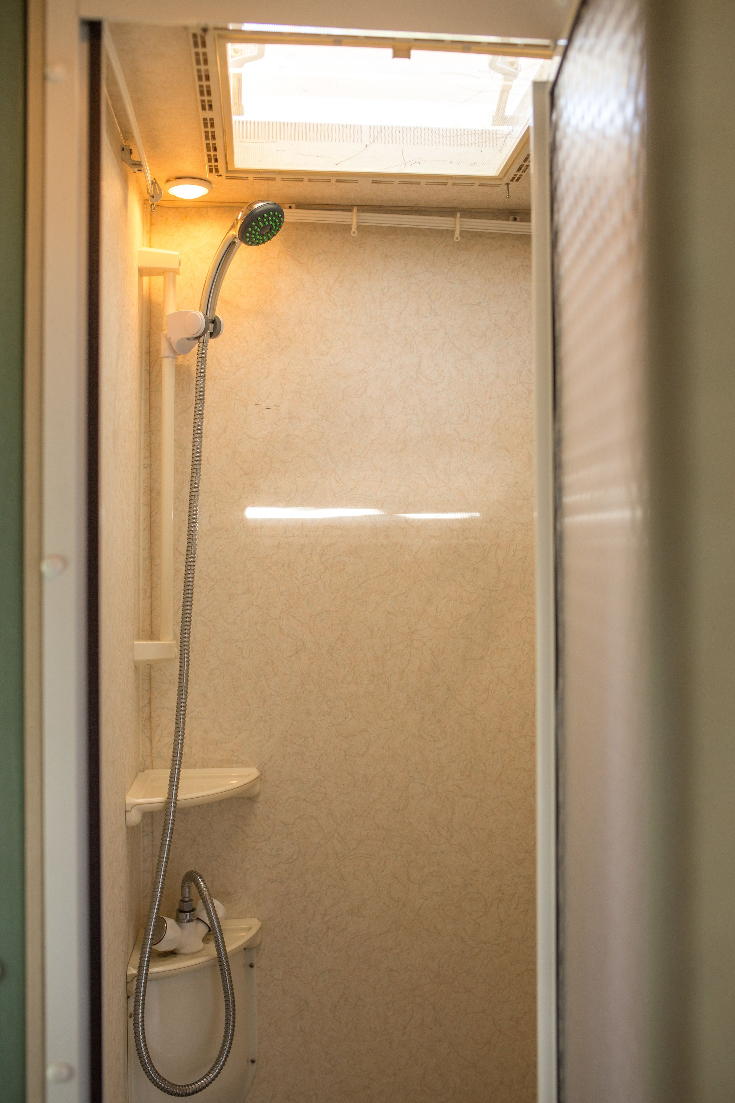 A small, enclosed shower area with a handheld showerhead and a wall-mounted faucet.