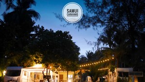Propiedad de Samui Caravans, con alojamiento en tienda de campaña, rodeada de árboles y luces colgantes.