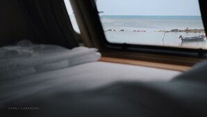 Vista desde una ventana, con una cama en primer plano y un mar tranquilo con barcos al fondo.
