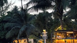 Un bar frente a la playa con un letrero que indica servicios como comida, café, cerveza artesanal y excursiones en barco.