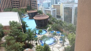 A rooftop pool area with two large circular water features, surrounded by palm trees and lounge chairs, set against a backdrop of high-rise buildings. - Eastern Suites at Times Square KL (Kuala Lumpur)