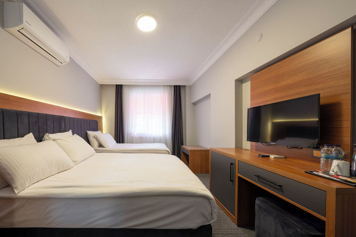 A hotel room with two beds, a TV, a desk, and a window with curtains.