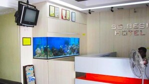 A hotel reception area with a large aquarium, a television mounted on the wall, and a reception desk with a red accent. - Sungai Besi Hotel (Seri Kembangan)