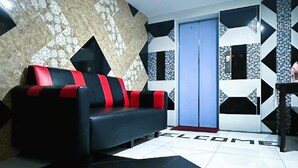 A modern living room with a black and red sofa, a patterned wall, and a tiled floor. - Sungai Besi Hotel (Seri Kembangan)