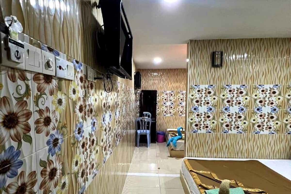 Une chambre d’hôtel avec un sol carrelé, un lit avec un oreiller vert, un téléviseur à écran plat fixé au mur et une petite table avec une chaise.