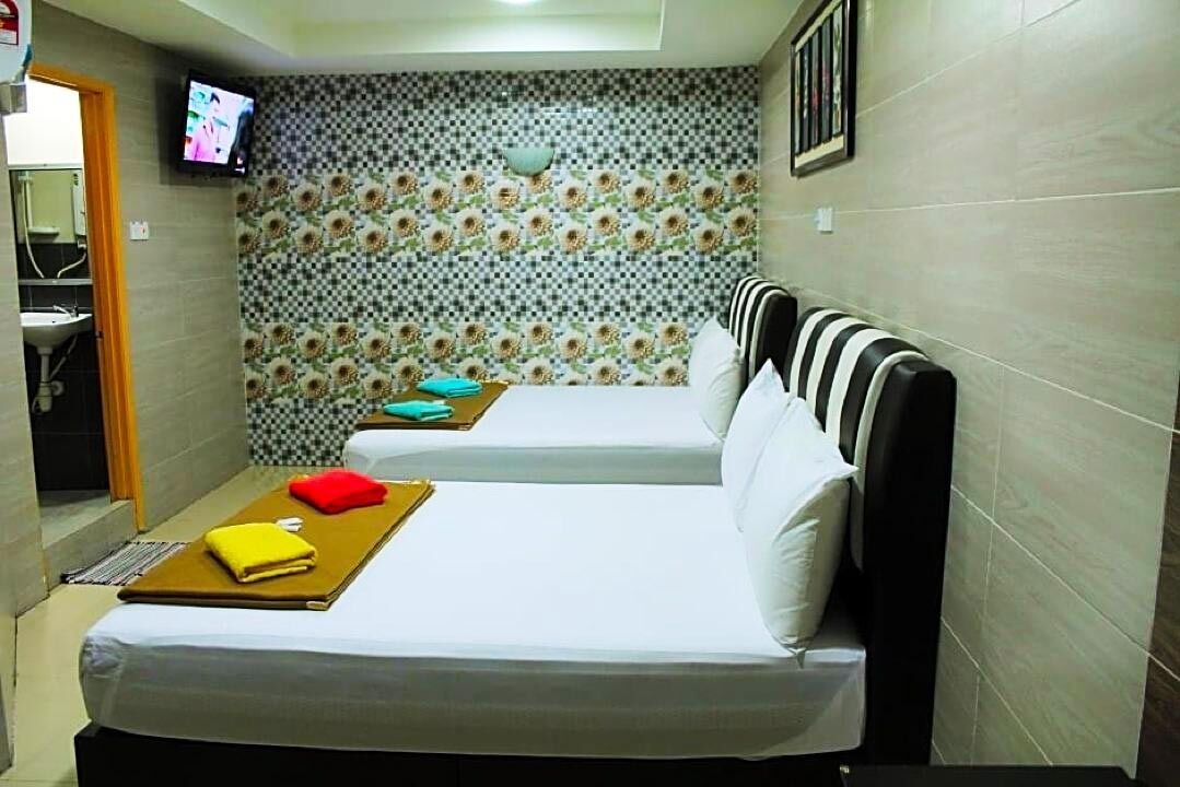 Habitació d'hotel petita amb dos llits, televisió, bany amb rentapans i un mur amb un disseny decoratiu.