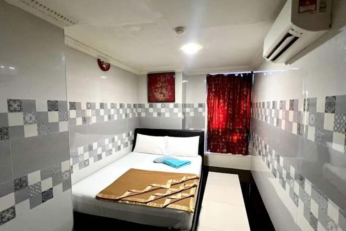 Une chambre d’hôtel avec un lit, un rideau rouge, un climatiseur fixé au mur et des carreaux à motifs.