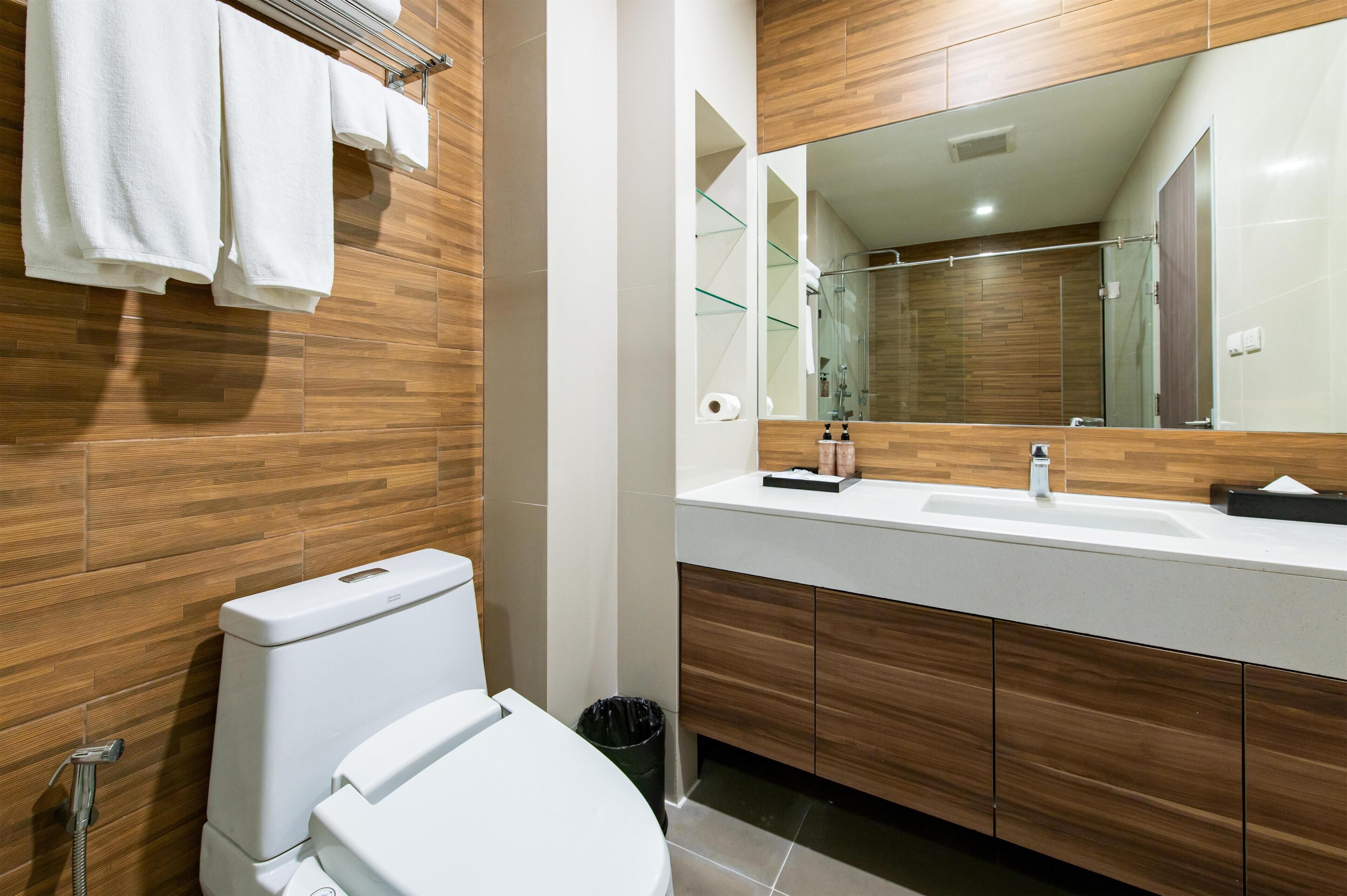 A modern bathroom with a wooden wall, a white toilet, a large mirror, and a white sink with a countertop.