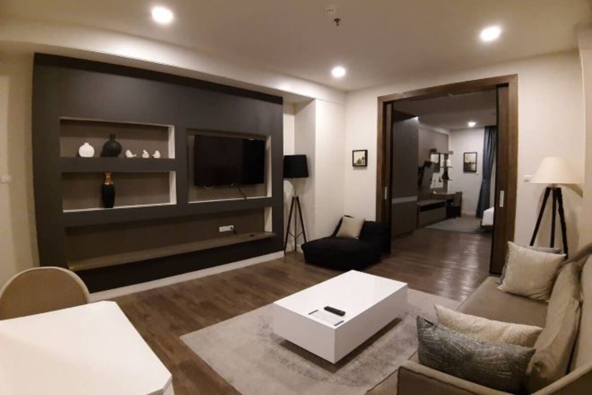 Uma sala de estar moderna com uma TV de tela plana, um sofá, uma mesa de centro e uma área de jantar com mesa e cadeiras.
