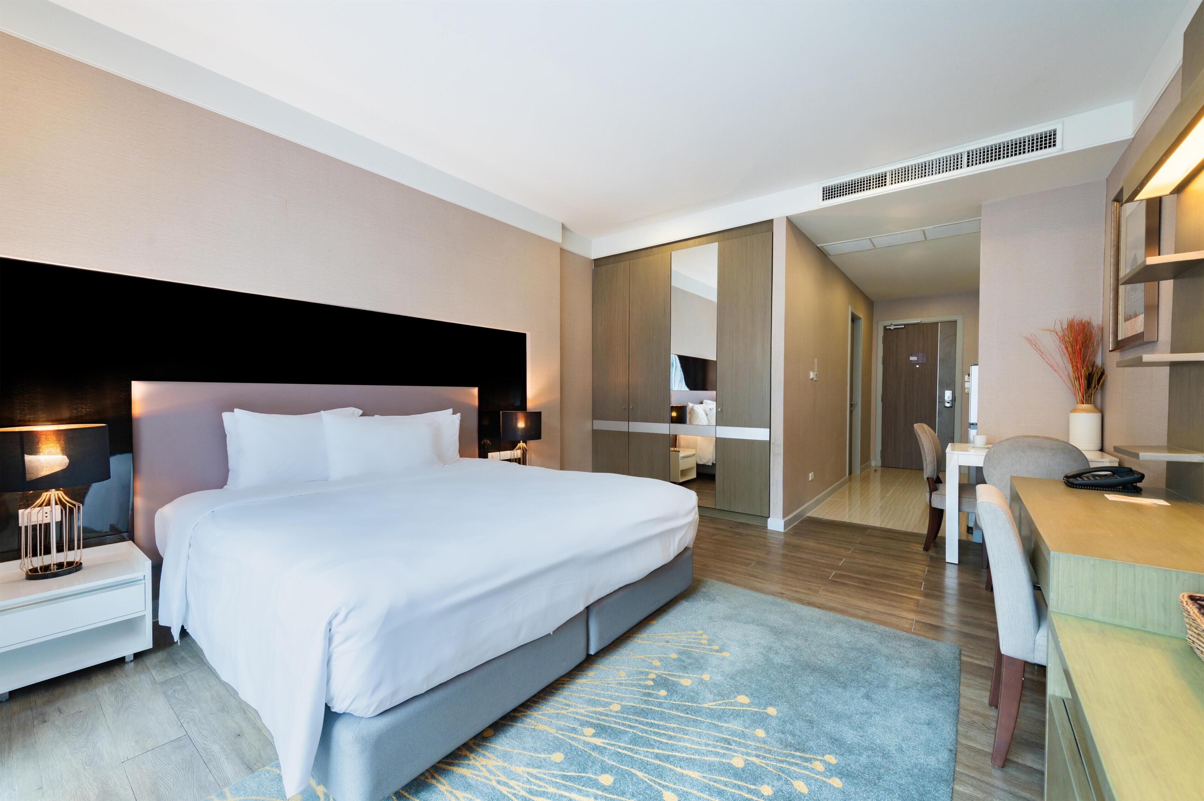 A modern hotel room with a large bed, bedside tables, a desk, and a mirror.