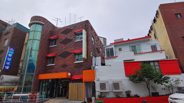 Un edificio de varios pisos con fachada de ladrillo, una estructura cilíndrica de vidrio y un edificio blanco con detalles en rojo.