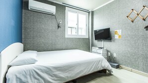 Un dormitorio moderno con cama, aire acondicionado, ventana, televisión y un pequeño escritorio con silla.
