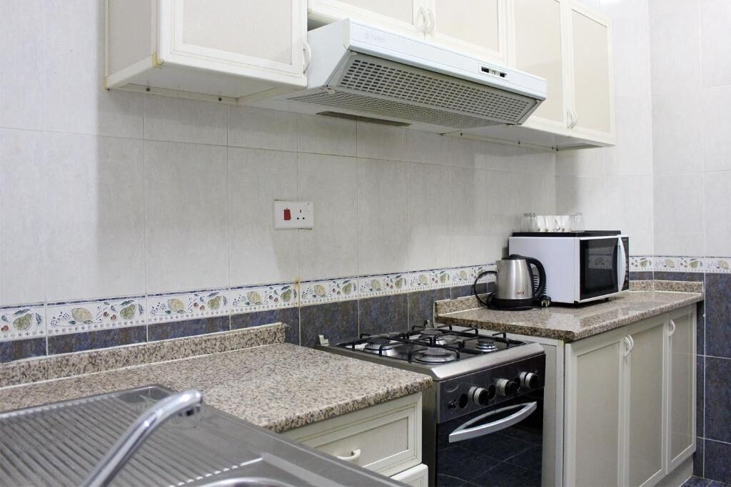 A kitchen with white cabinets, a gas stove, a microwave, and a kettle on the countertop.