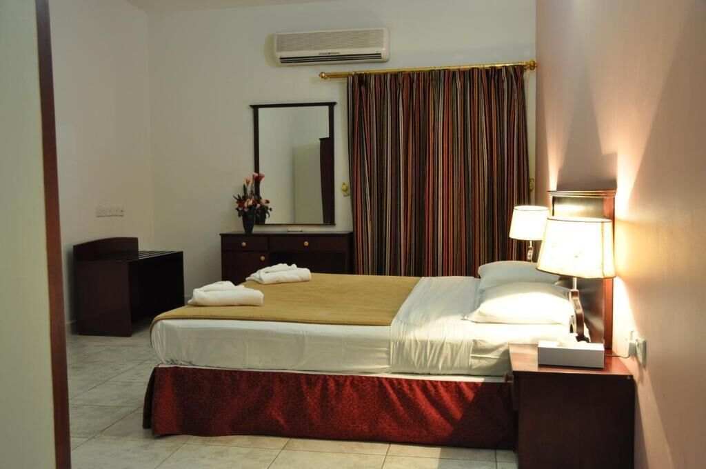 A hotel room with a bed, a nightstand, a lamp, a mirror, a dresser, and a curtain.