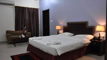 Una habitación de hotel con cama, mesita de noche, lámpara, sofá y ventana con cortinas.