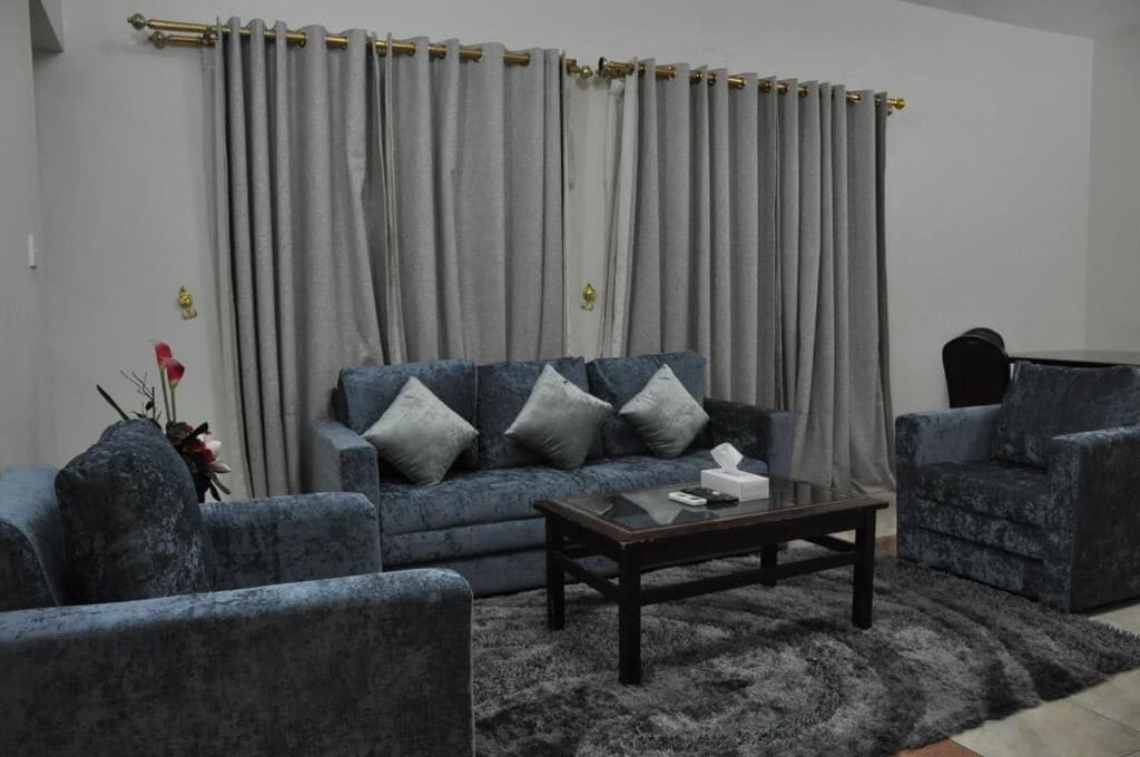 Un salon avec un canapé gris, deux fauteuils, une table basse et un rideau gris.