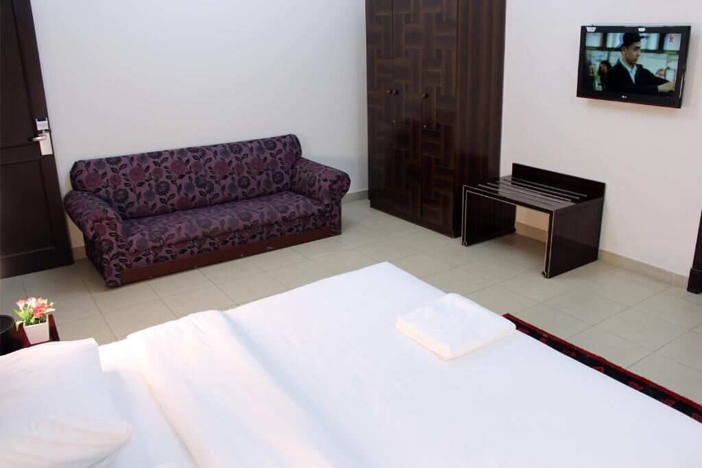 A hotel room with a bed, a sofa, a TV, and a wardrobe.