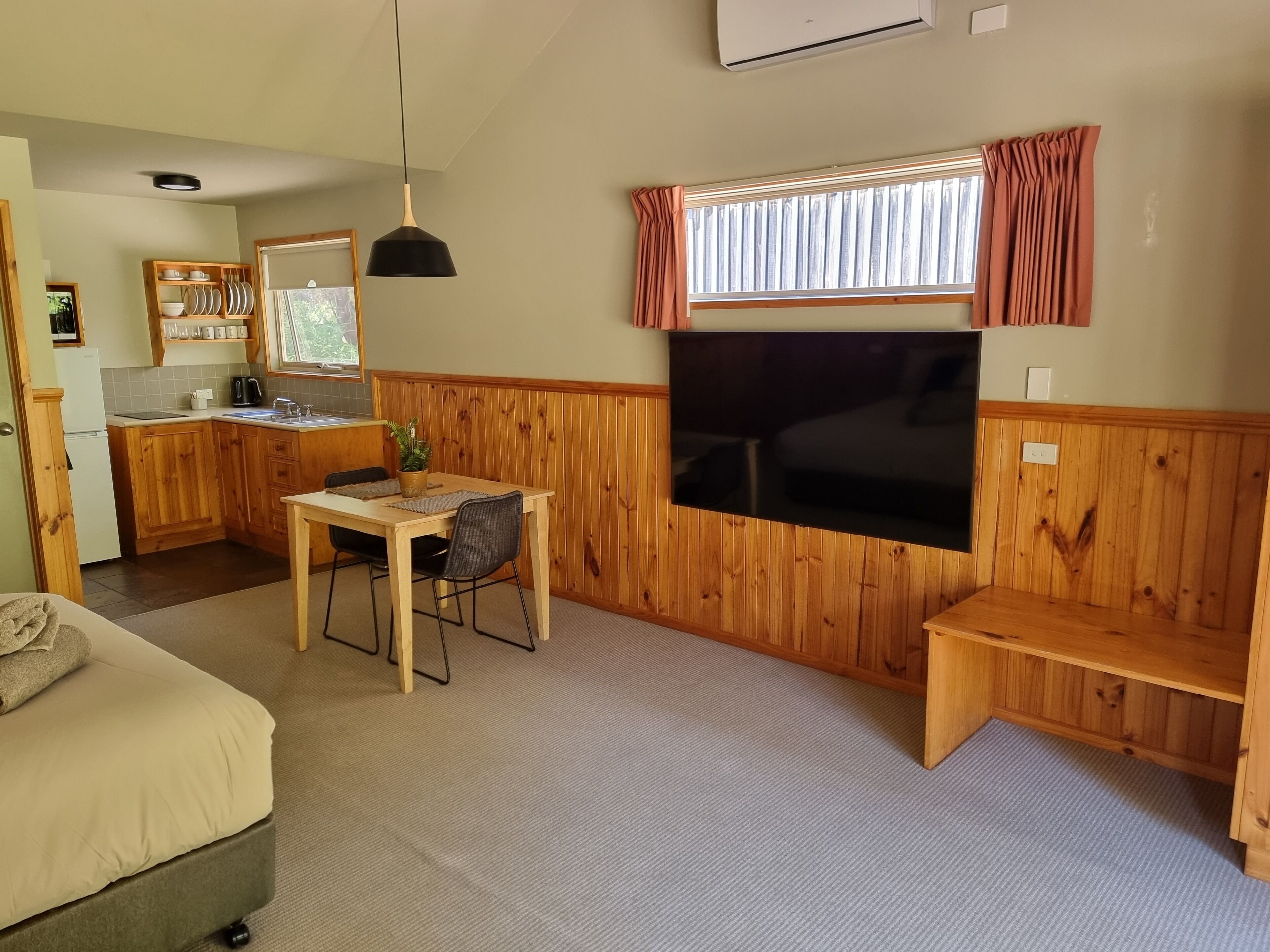 A compact living space with a kitchenette, a dining area, a seating area, and a TV mounted on the wall.