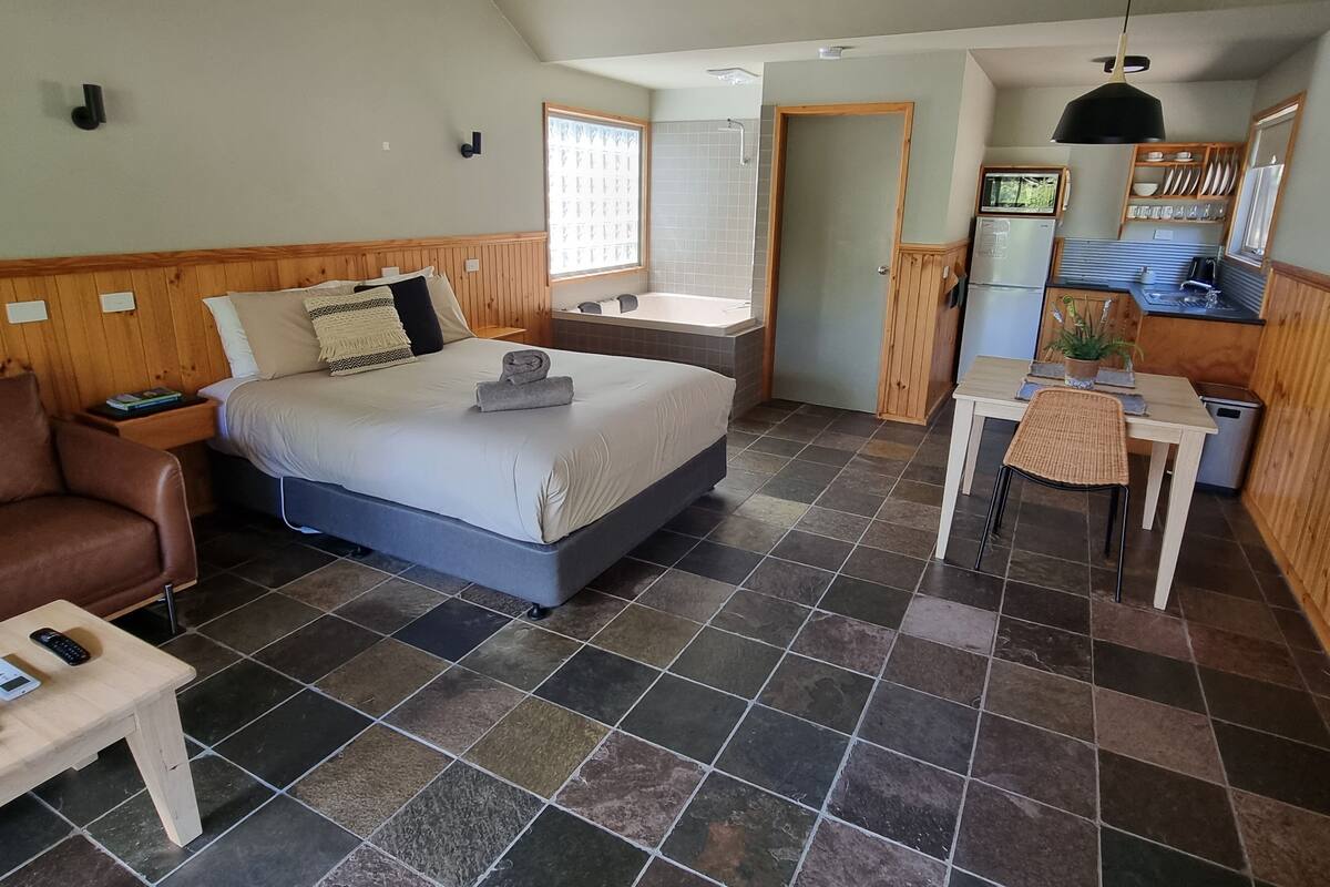 A bedroom with a bed, bedside table, chair, and a small table with a plant.