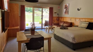 A hotel room with a bed, a desk, a chair, a table, and a large window with curtains.