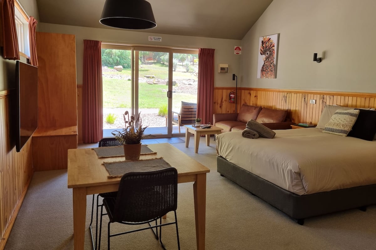 A hotel room with a bed, a desk, a chair, a table, and a large window with curtains.