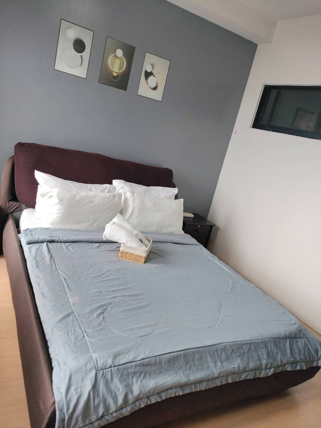 Un letto rifatto con cura, con copripiumino blu e cuscini bianchi, una testiera marrone scuro e un comodino con una lampada.