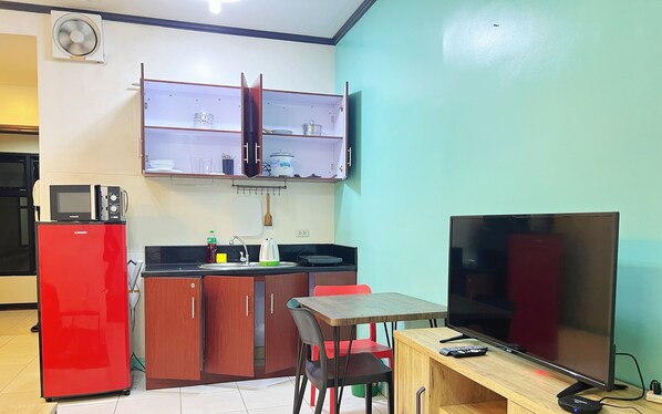 Una cocina compacta con microondas, lavamanos y una pequeña zona de comedor con televisor.