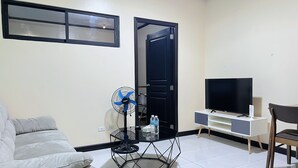 A living room with a sofa, a glass-top coffee table, a TV on a stand, a fan, and a door. - Serena's House - Manila (Manila)