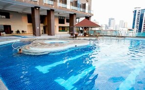 Una piscina con hidromasaje, una zona de estar techada y vistas a un paisaje urbano.
