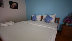 A neatly made bed with white linens and blue pillows, a wooden nightstand with a vase of flowers, and a painting on the wall. - Sweethome Resort (Surin)