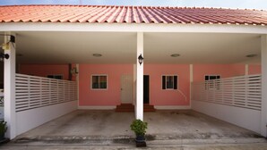 A building with a red-tiled roof, a pink facade, and a covered entrance area with steps leading to a door. - Sweethome Resort (Surin)